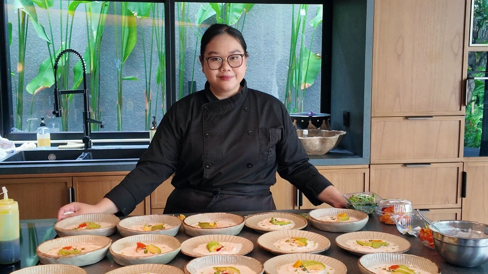 A chef wearing glasses preparing rows of plated dishes in a villa kitchen