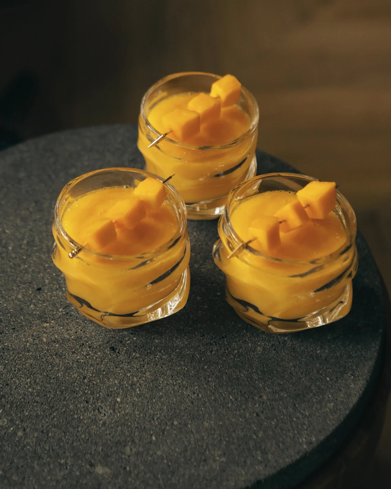 Three desserts in glasses topped with yellow fruit