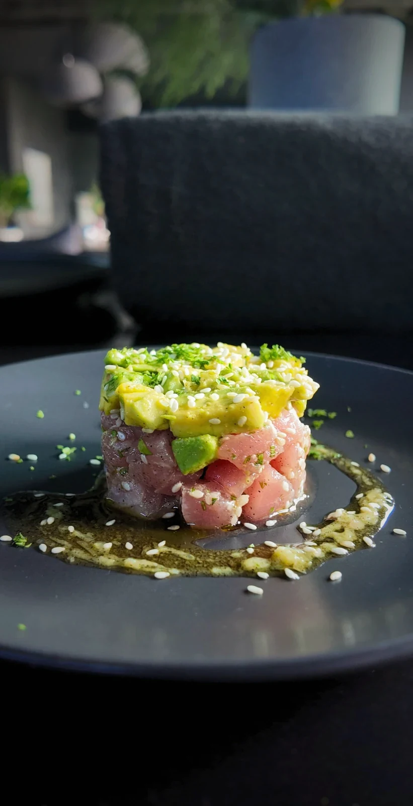 Fish tartare topped with avocado and sesame on a dark plate