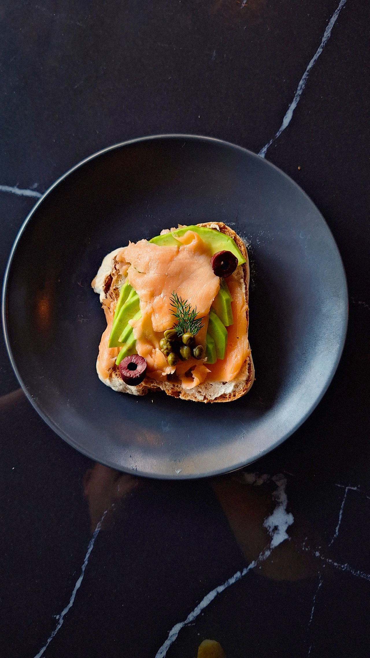 Smoked salmon and avocado on toast, served on a dark plate